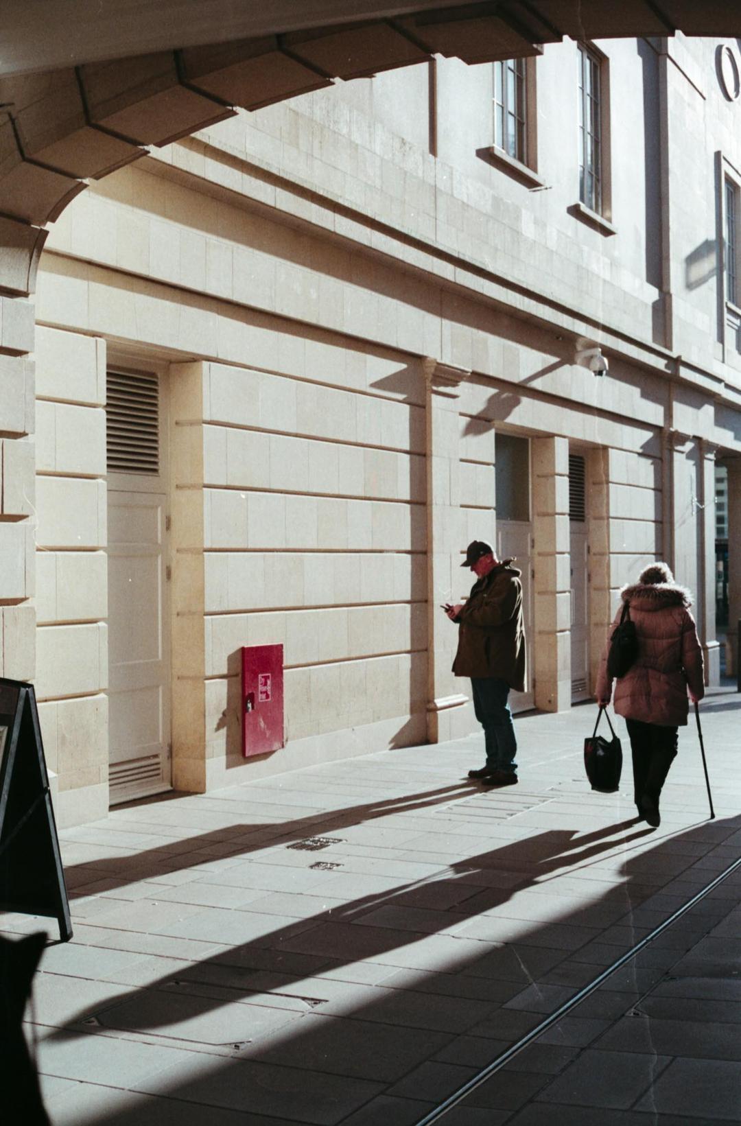People walking along a street with long late-day shadows