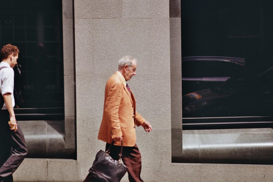 An older man in a bright orange coat walking through the city